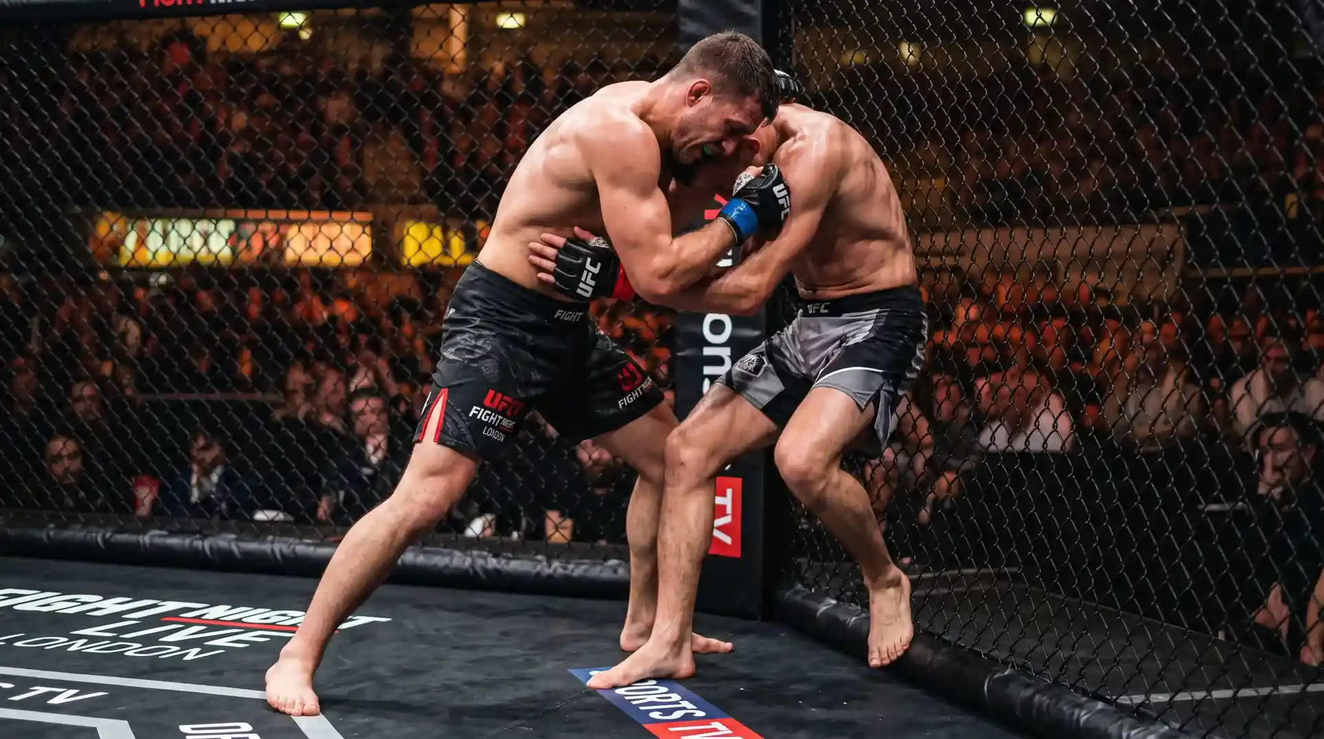 Two MMA fighters exchanging strikes inside a cage at a UK event